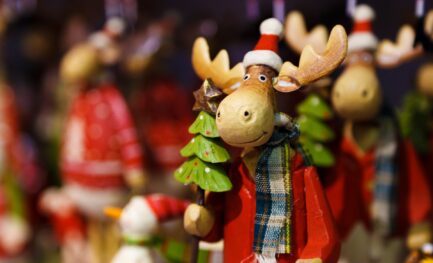 Handcrafted wooden moose figurine wearing winter clothing and holding a small Christmas tree, used decoratively on the Perry Hall Craft Fair homepage.